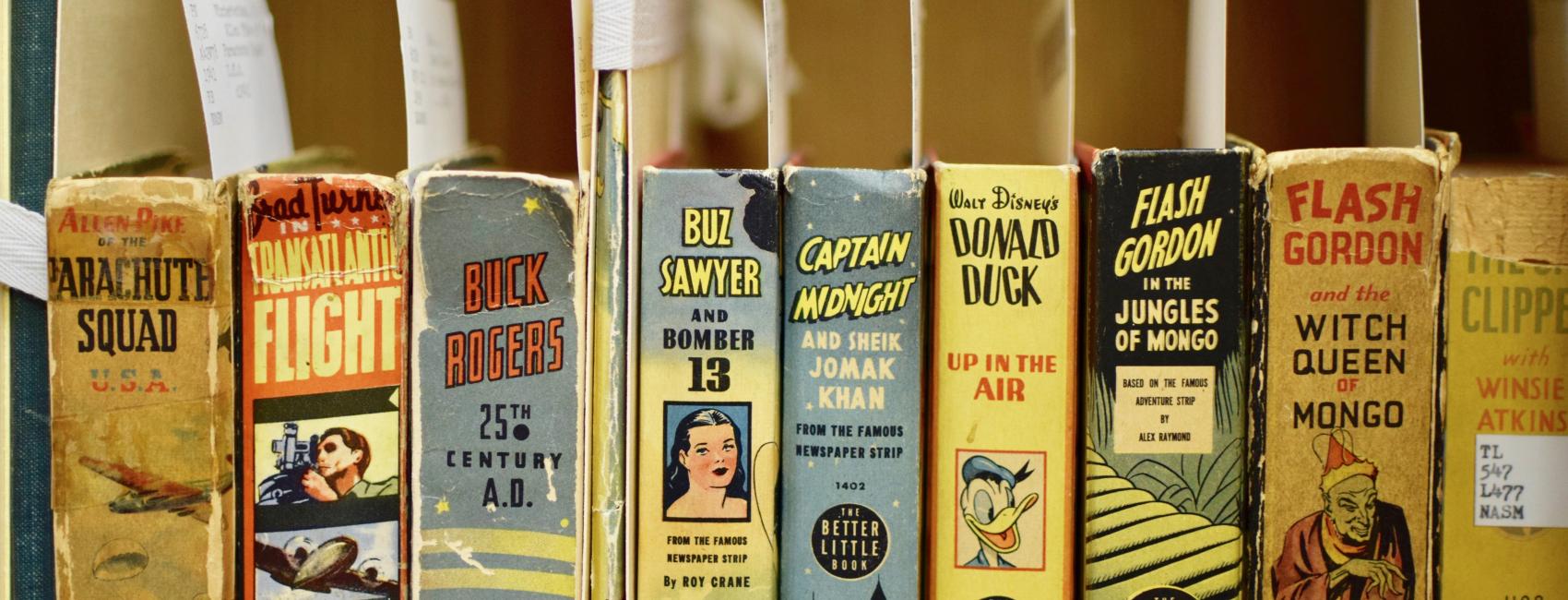 A row of short squat books with index cards peeking out. The books stand up with the spines facing out. Each spine is colorful and boasts a comic like "Flash Gordon," Buck Rodgers," or "Donald Duck Up in the Air."