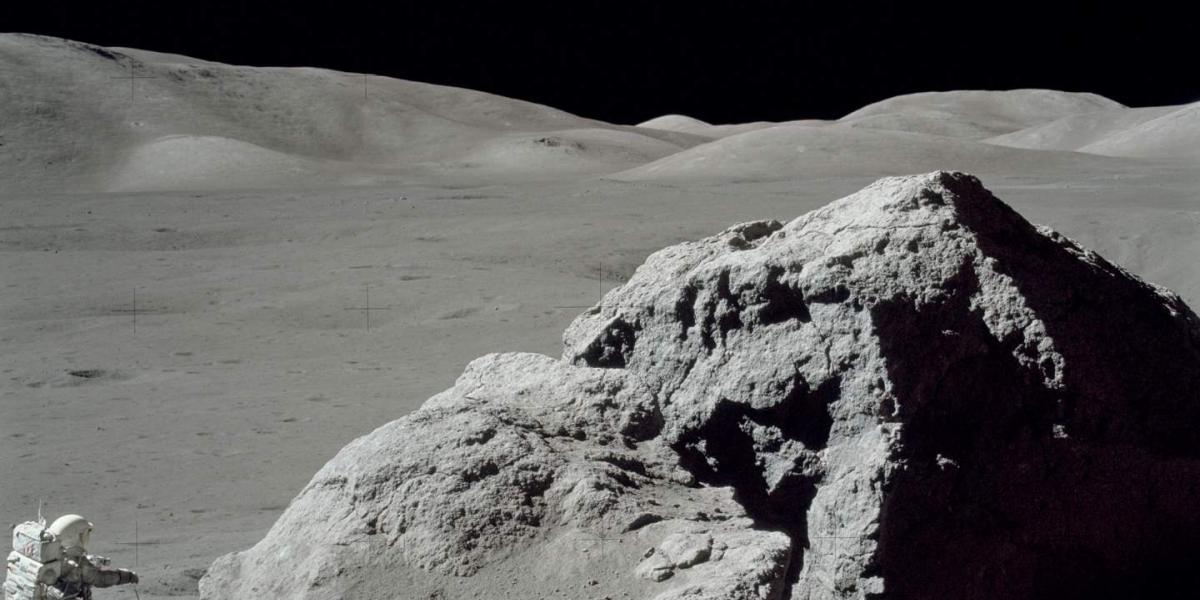 An astronaut by a huge rock on the moon.