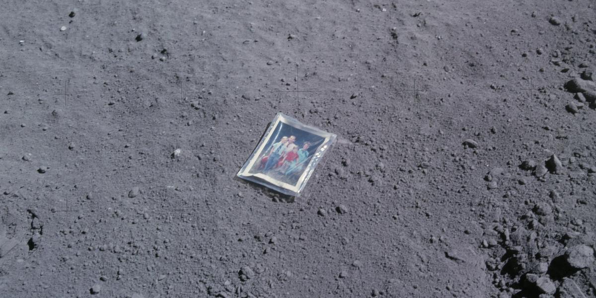 A photo of a framed photo of a family laying on the surface of the Moon.