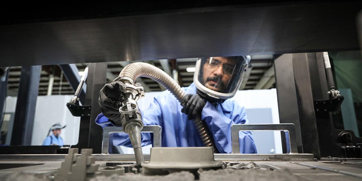 Manufacturing Engineer with face shield holds a nozzle to make an aircraft part 