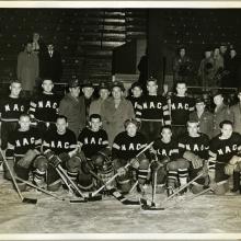 A group of men pose wearing hockey uniforms. Some of the men are holding hockey sticks.