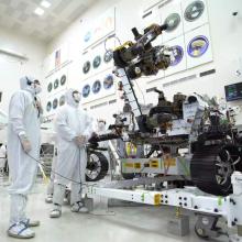 Three people in white protective suits work on rover