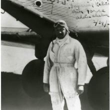 A black and white photograph of a man standing in front of a plane.