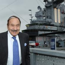 A man stands smiling in front of a ship. 