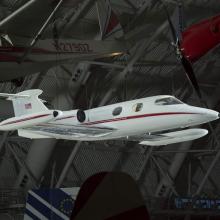 White, twin-engine business jet with red stripe and metallic wings, hanging in dim interior