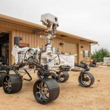 A car sized rover with six wheels sit outside a garage.