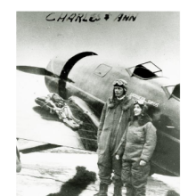 Charles and Anne Lindbergh stand on side of their Lockheed Sirius while wearing aviator gear.