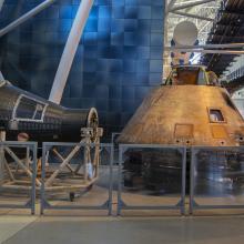 Two capsules that traveled in space, one larger than the other. Both are conically shaped.