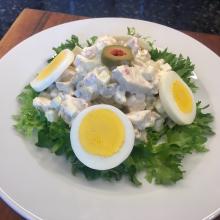 Photograph of chicken salad on white plate with a bed of lettuce, hard boiled egg cut in half, and green olives