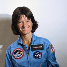 Sally ride in a blue astronaut jumpsuit holding a helmet