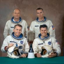 four men seated in two rows in spacesuits