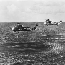 two helicopters fly over water