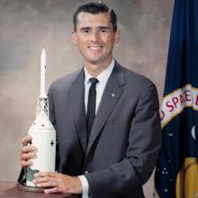 A color photographed portrait of Roger B. Chaffee holding a model of a rocket.