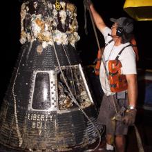 Man stands next to a space capsule recently removed from the ocean