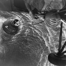 view of helicopter attempting to lift spacecraft partially submerged in ocean