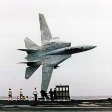 A jet flying sideways over an naval carrier