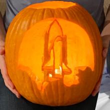 Two pumpkins decorated with space themes, one showing a space shuttle launching and the other showing constellations.