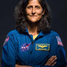 A woman in a flight suit with the name tag Suni Williams. Her arms are crossed. 