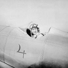 A woman in the cockpit of a plane looks behind her.