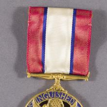 A round medal on a red, white, and blue ribbon. The medal has an eagle on it and text that reads "For Distinguished Service."