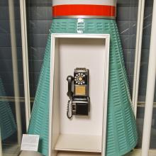 A phonebooth in turquoise color that is shaped like a space capsule with a dial phone in the middle.