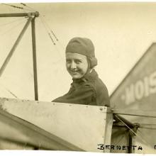 A woman smiles from the cockpit of an airplane.