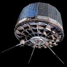 A column shaped satellite with metallic panels on the sides and three prongs emerging from the bottom.