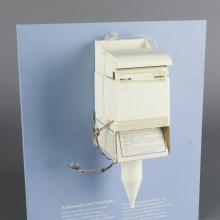 A white device that looks like a mailbox or soap dispenser with a pointed cone emerging from the bottom.