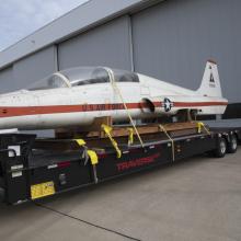 A woman examines a T-38 Talon aircraft while it's strapped to the back of a truck without its landing gears.