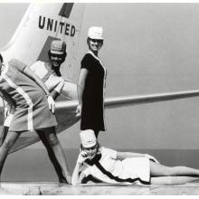 A black and white photograph of four female flight attendants posing in various positions in front of an aircraft.