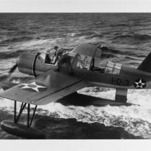 Black and white image of an airplane riding on top of water with a man on its wing.