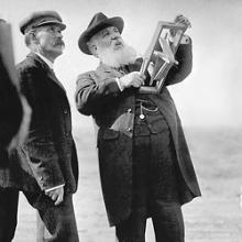 Alexander Graham Bell holding the handle of a kite and looking up into the air.