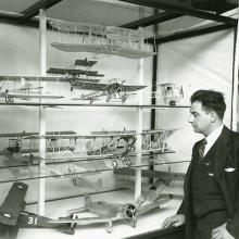 Paul Garber dressed in a suit looking at a cabinet containing airplane models.