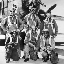 Black and white photograph of six Black men in flight gear (three in front and three in back) posing in front of an aircraft nose.