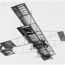 Side view of an airplane in flight. The initials A.C.F. can be seen on the bottom of the plane.