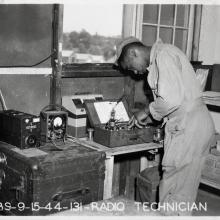 Black and white photograph of a man in uniform standing in front of radio equipment