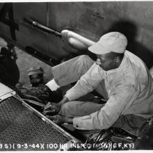 black and white photograph of black man in uniform sitting on a wing and working on an engine