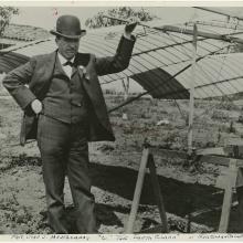 A photo of John Montgomery standing next to a glider. One hand is on the glider and the other is on his hip.