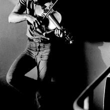 A man playing a violin while leaning on a wall