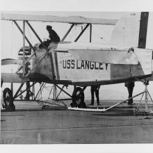 Black and white grainy image of an aircraft with someone sitting on top.