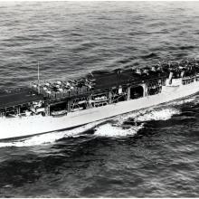 An old photograph of a long oval boat on the water. 