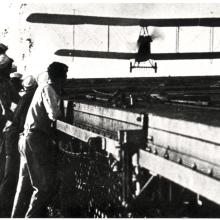 Several individuals lean over a railing watching an airplane land. 