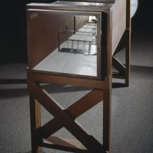 Wooden frame supporting hollow rectangular box-shaped wind tunnel.