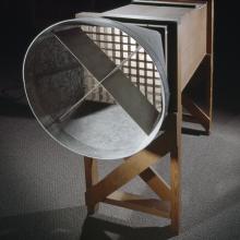 A wind tunnel with a metal circular piece attached to hollow rectangular box-shaped wind tunnel on wooden frame.