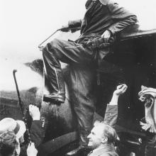 A woman stand by the wing of an aircraft, smiling, while others surround her.