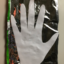 A cut out of white printer paper in the shape of a hand, lying on a piece of mylar. 