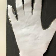 A cut out of a hand on printer paper, stacked on a cut of of a hand on Mylar, on top of a piece of black foam. 