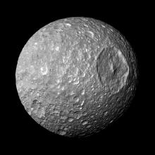 A rough grey sphere with a major circular crater on the upper right hand side. 