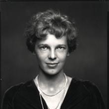 A half body portrait shot of a woman with short hair. One of her necklace has a pendant that looks like wings.