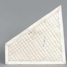 A quadrilateral (four-sided) piece of white quilted fabric. Serial numbers are written on the center of the piece. 